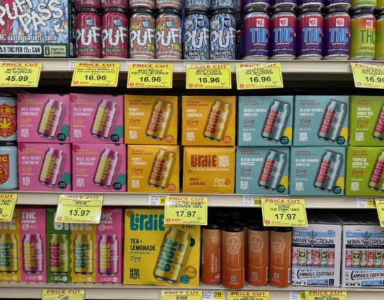 Shelves in a store display various cannabis-infused beverages and products, each labeled with price tags indicating discounts.
